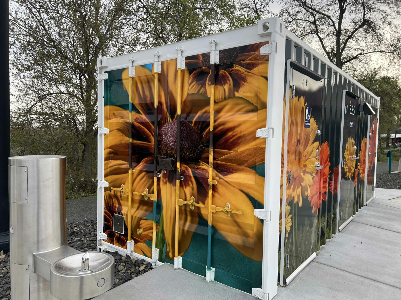 Vinyl wraps featuring colorful floral imagery cover the outside of a shipping container restroom at Columbia Gardens Wine & Artisan Village.