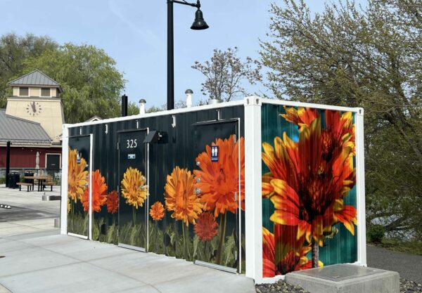 Vinyl wraps featuring colorful floral imagery cover the outside of a shipping container restroom at Columbia Gardens Wine & Artisan Village.