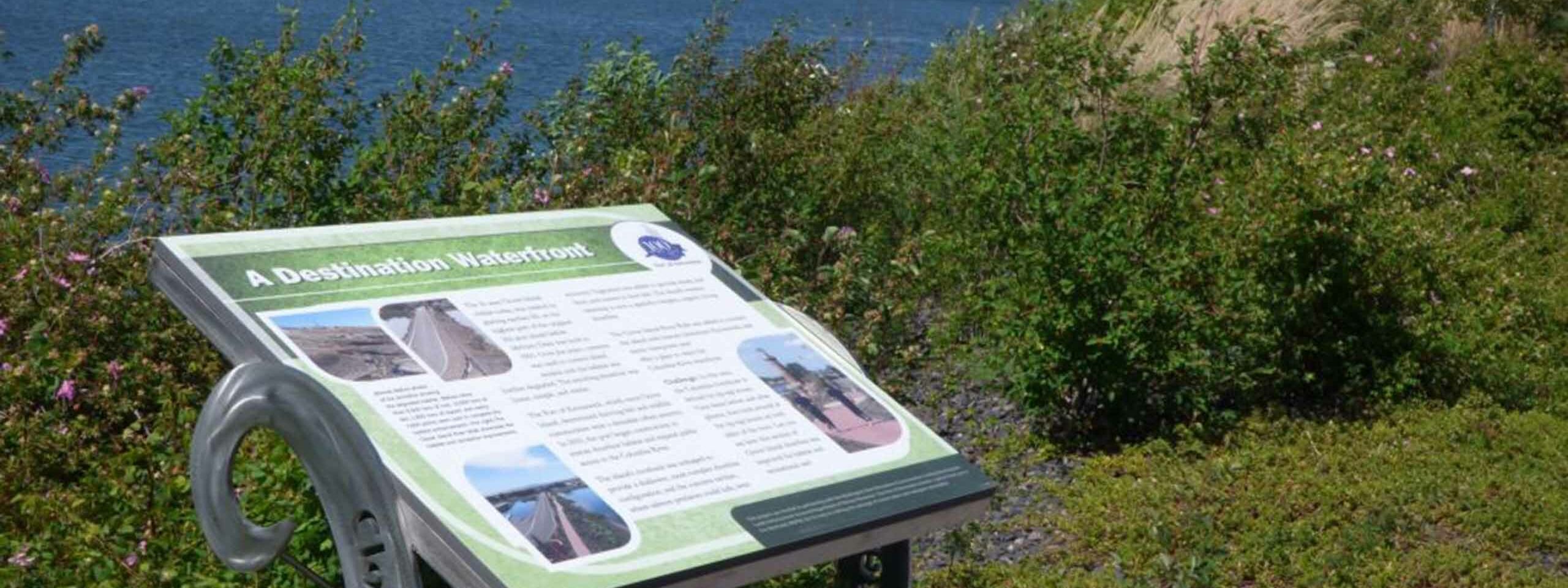 An educational panel along the Clover Island Riverwalk trail with the Clover Island Lighthouse in the distant background.